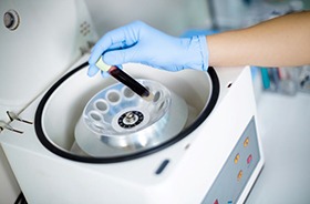 Gloved hand placing vial of blood into centrifuge