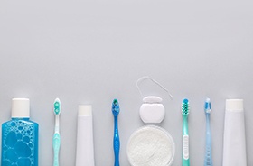 Toothbrushes, toothpaste, and floss lined up against neutral background