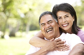 Happy couple with dental implants in Hamden laughing outside