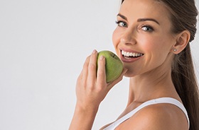 Woman with dental implants in Hamden smiles while eating an apple