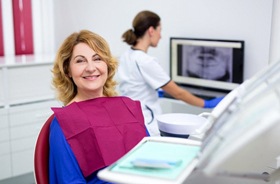 An older woman sitting in the dentist’s chair while the dentist reviews x-ray images