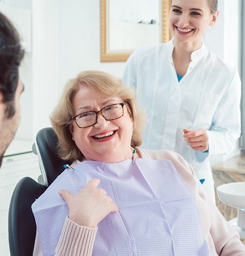 Older woman in dental chair smiling at dental team member