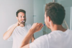 Man brushing his teeth to reduce risk of dental implant failure