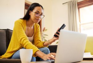 Woman using computer and phone to search for emergency dentist